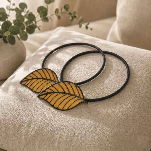 Two matching yellow leaf tiebacks styled together on a linen cushion