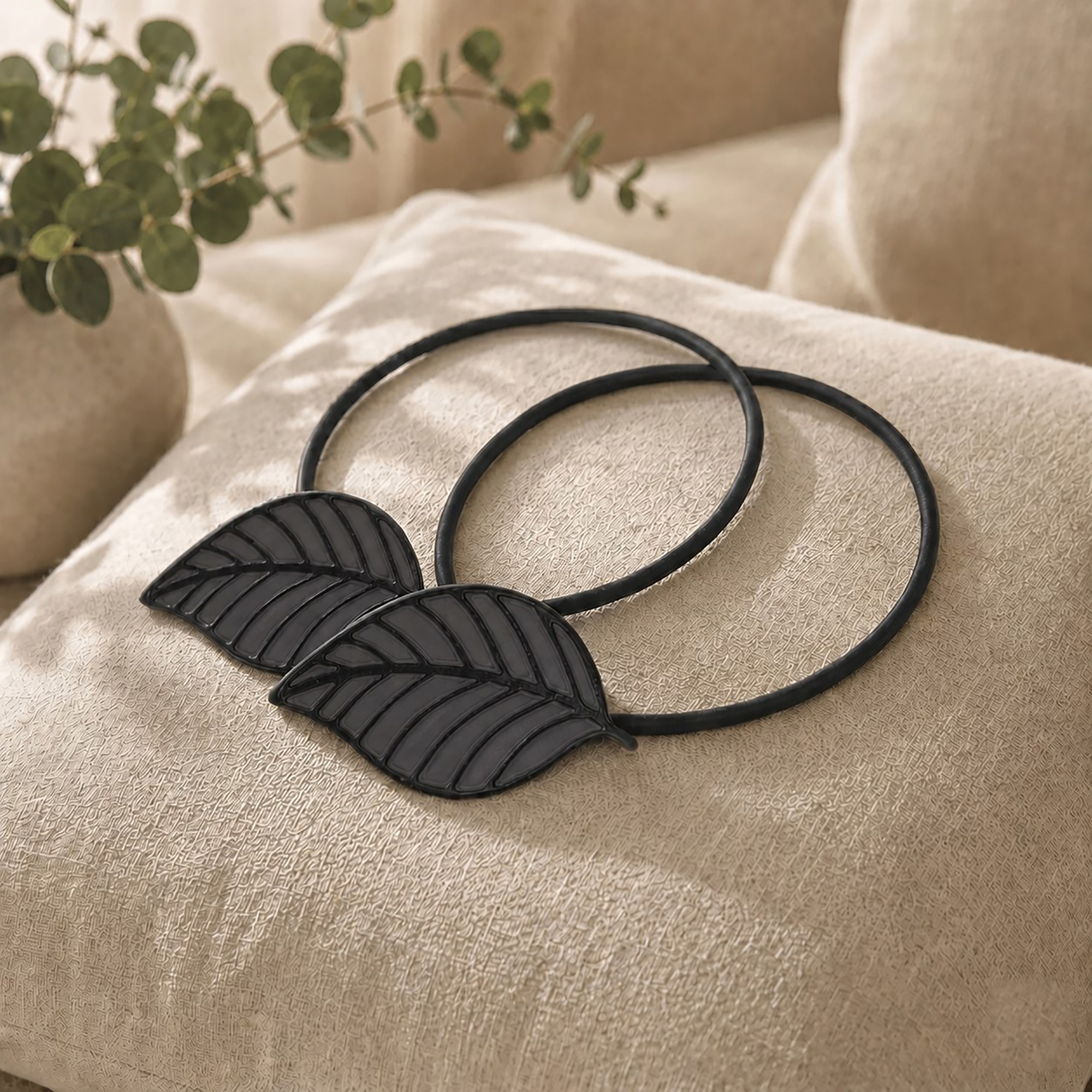 Two matching gray leaf tiebacks styled together on a linen cushion