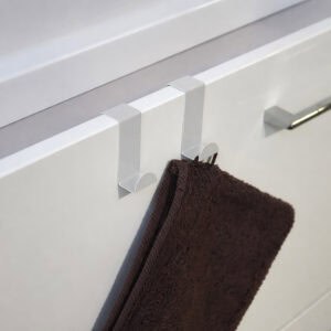 "Two white over-cabinet hooks holding dark brown towel on white bathroom vanity drawer"