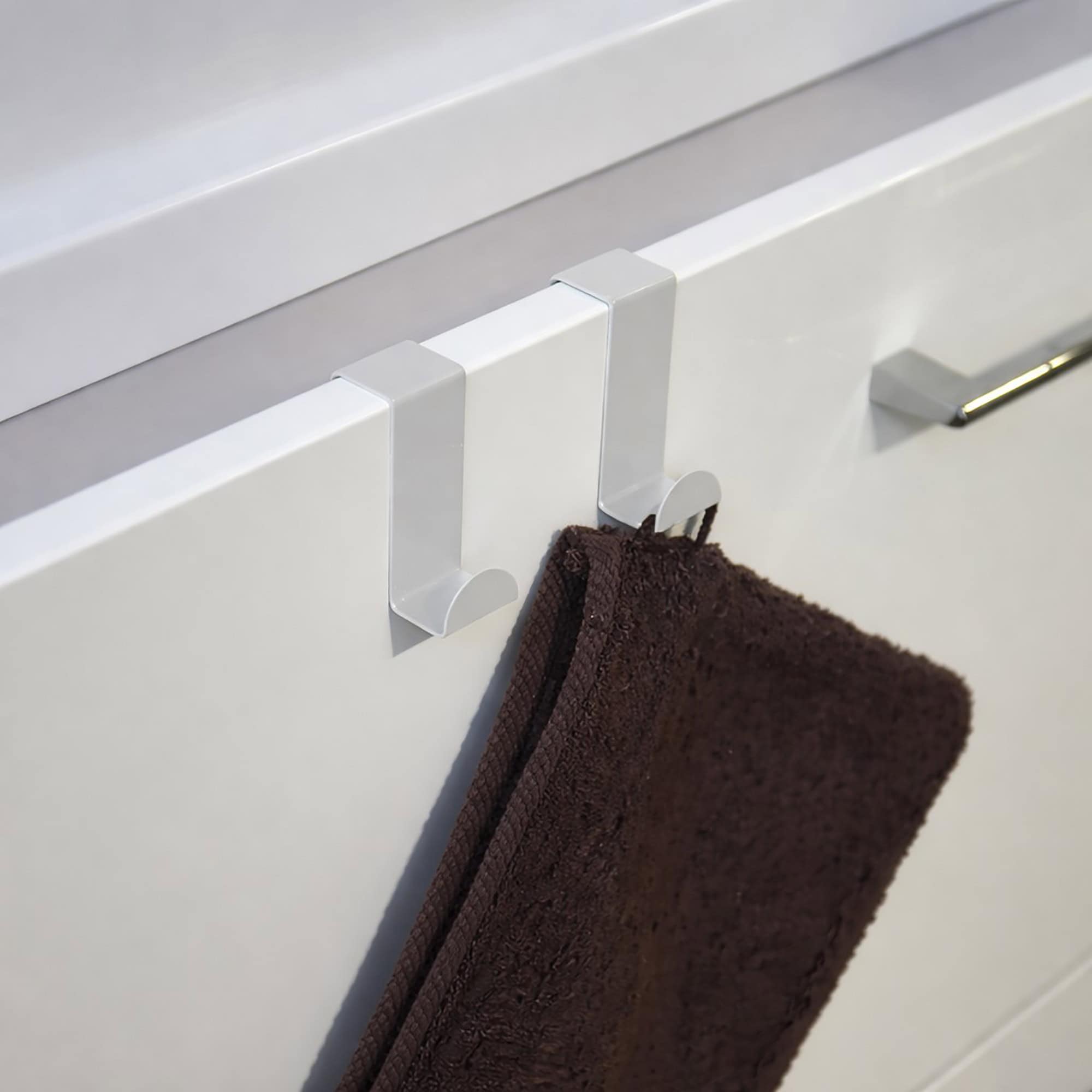 "Two white over-cabinet hooks holding dark brown towel on white bathroom vanity drawer"