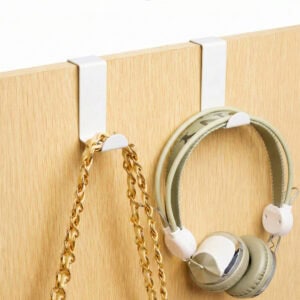 "Two white over-cabinet hooks on wood door holding gold chain necklace and green headphones"