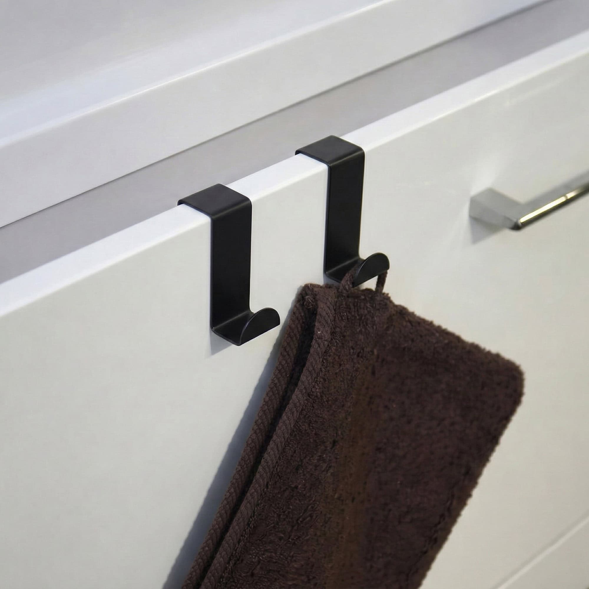 "Two black hooks on white cabinet door holding a brown towel"
