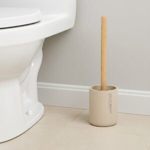 Beige toilet brush with bamboo handle in matching holder placed beside toilet