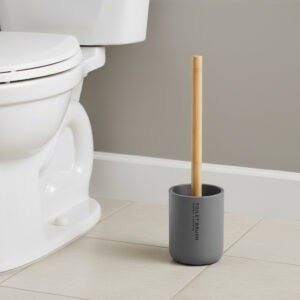 Gray toilet brush with bamboo handle in matching holder placed beside toilet