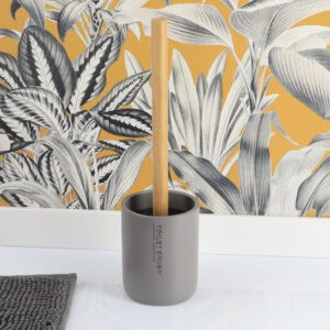 Gray toilet brush and holder displayed on bathroom floor with botanical wallpaper backdrop
