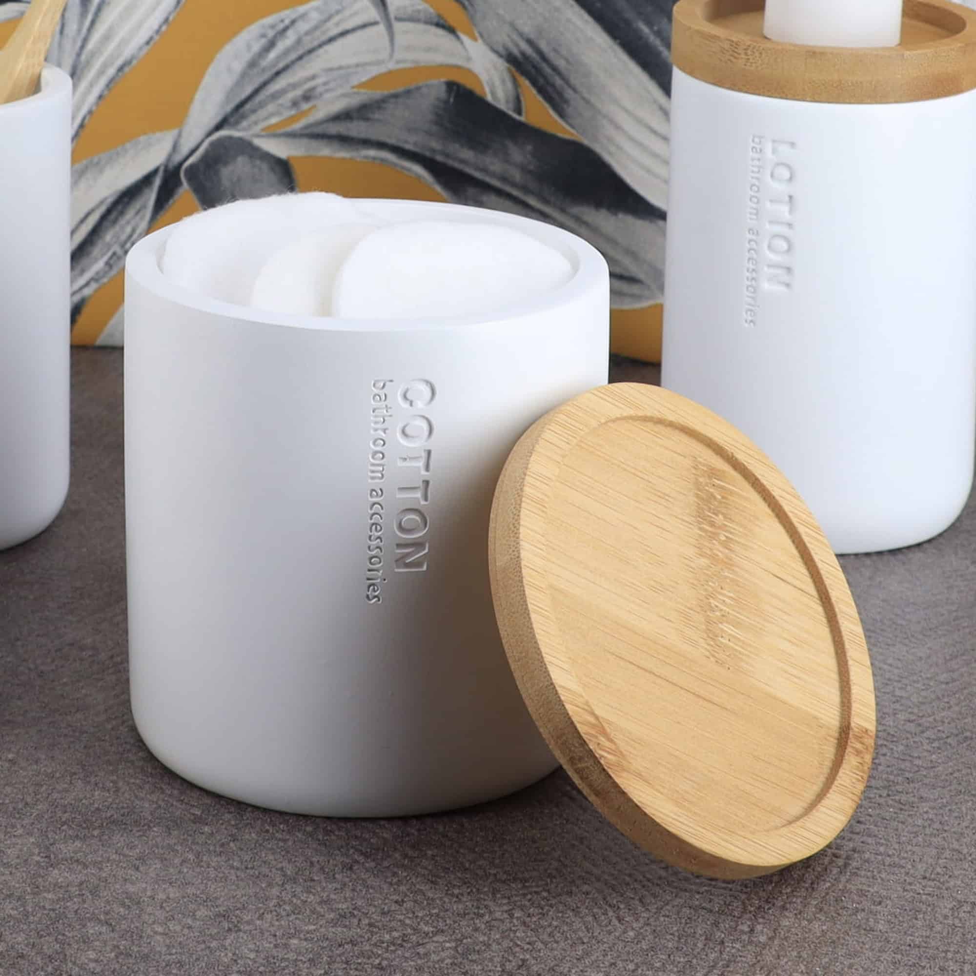 White cotton jar with removable bamboo lid showing cotton balls inside, part of matching bathroom set