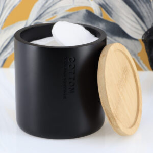Black cotton jar with bamboo lid removed showing cotton balls inside against tropical leaf wallpaper