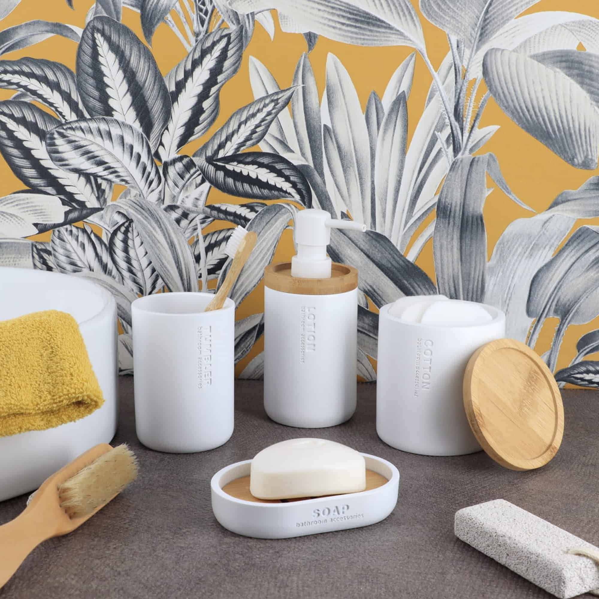 White bathroom accessories styled together with bamboo accents, including a lotion dispenser, tumbler, soap dish, and cotton jar.