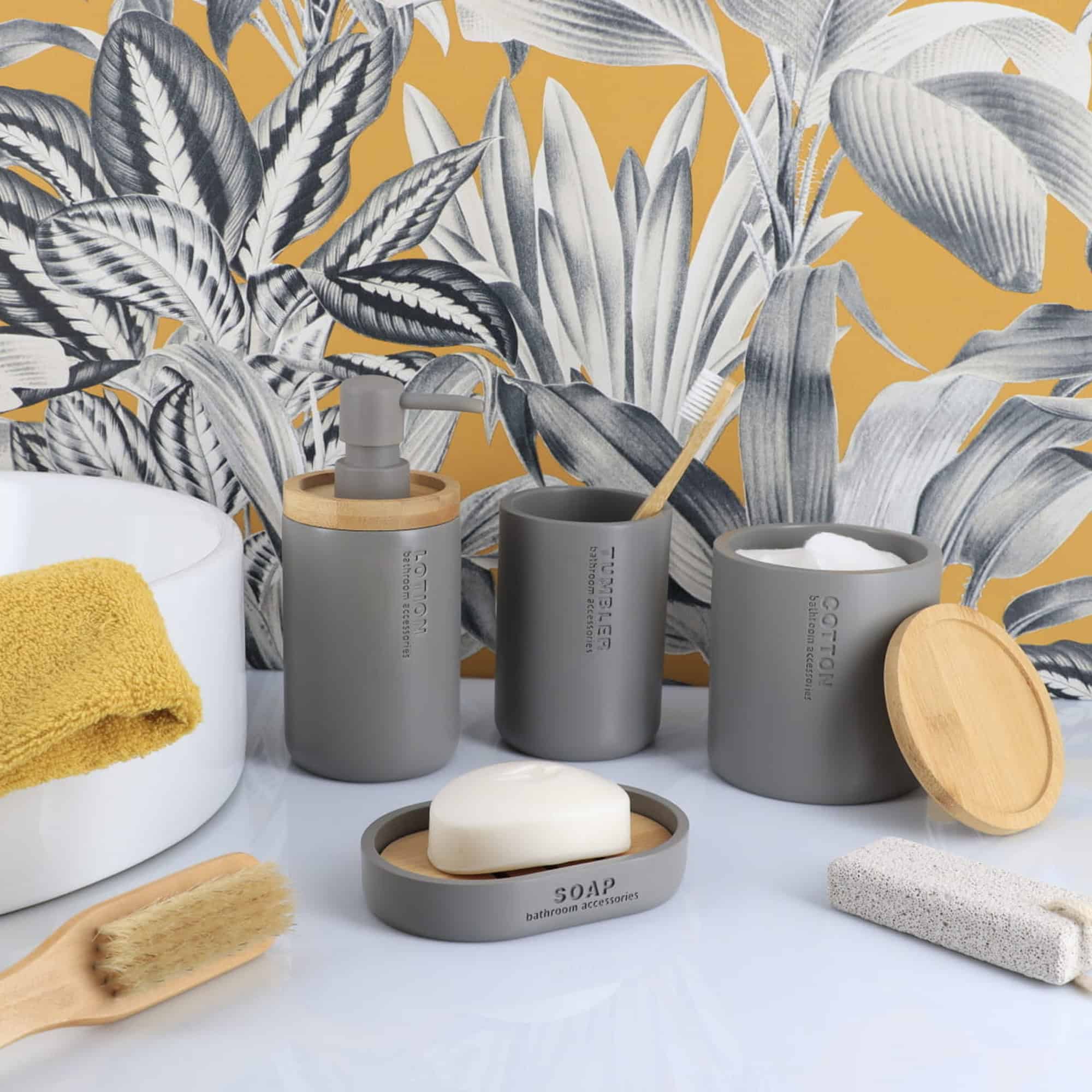 Gray bathroom accessories styled together with bamboo accents, including a lotion dispenser, tumbler, soap dish, and cotton jar.