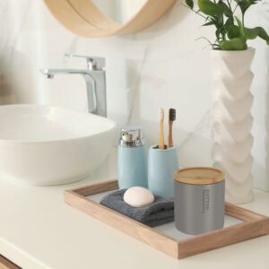 Matte gray cotton jar with bamboo lid on bathroom vanity tray with blue accessories and geometric planter