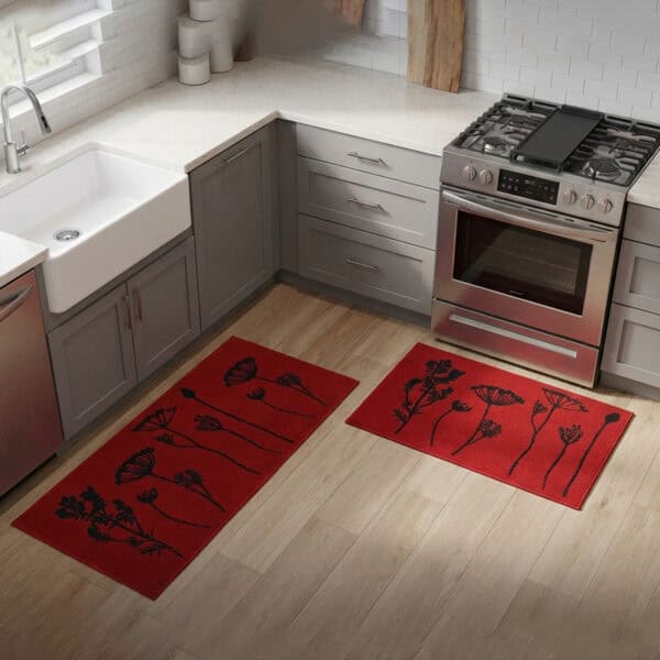 Red floral mat and runner set placed on hardwood beside a farmhouse sink and stove, black botanical stems adding a bold accent to the kitchen.