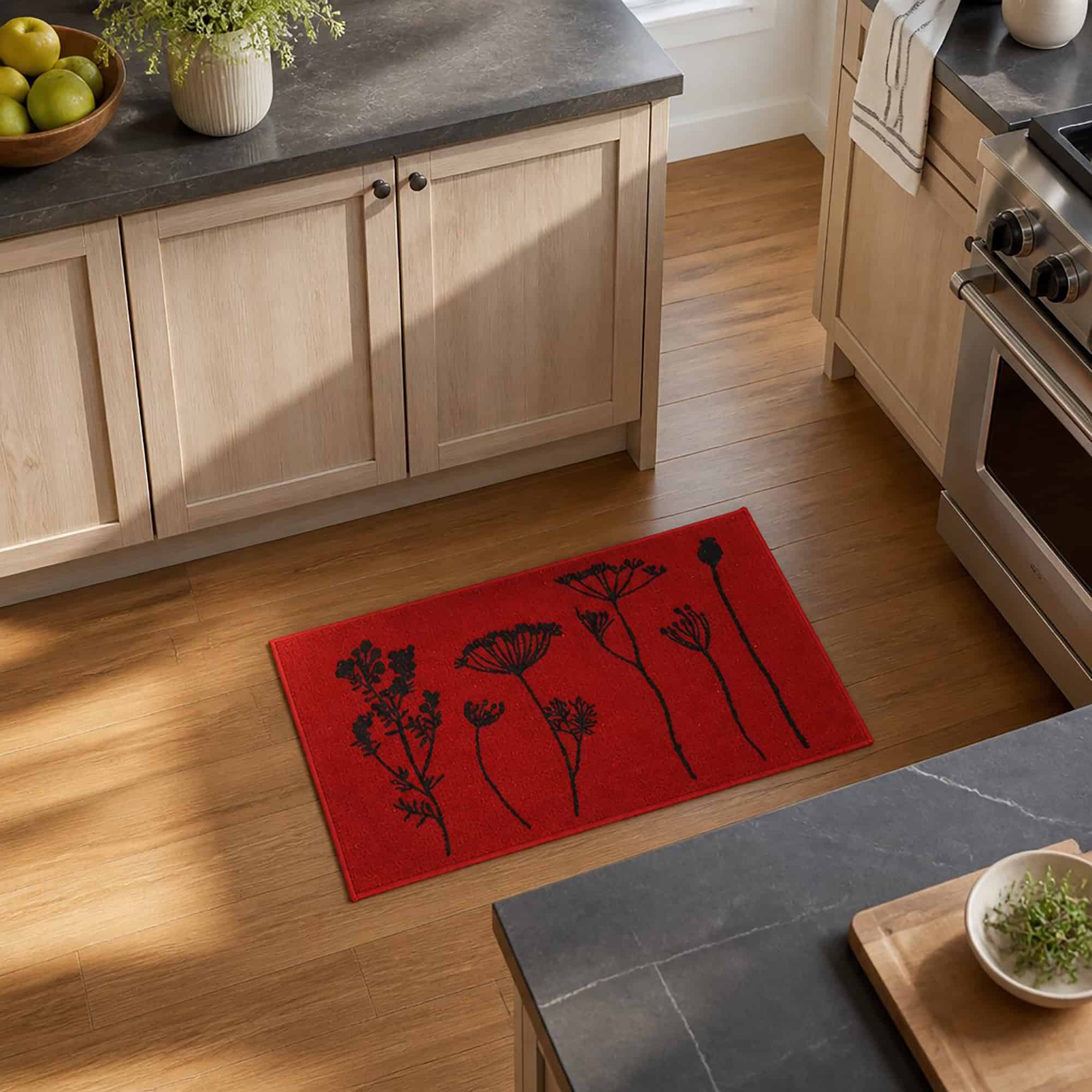 Red kitchen rug with floral print laid on warm hardwood flooring beside wood cabinets and a stainless range in a bright kitchen.