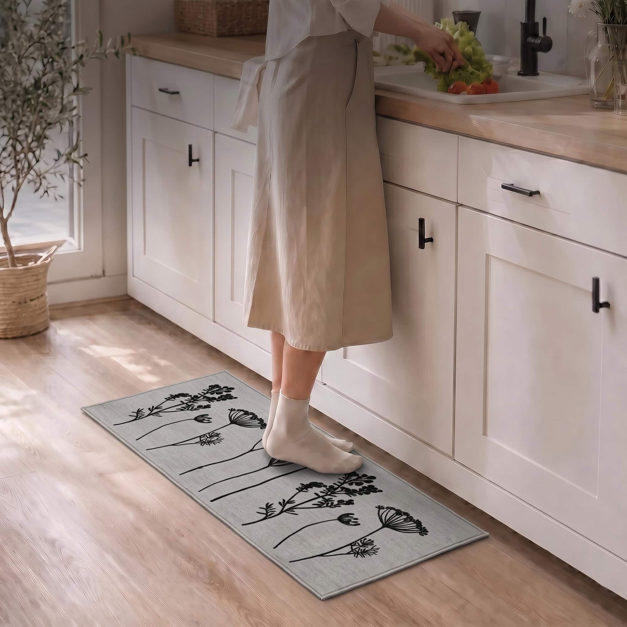 Woman in socks standing on a gray floral kitchen runner at the sink while preparing fresh produce in a bright modern kitchen.