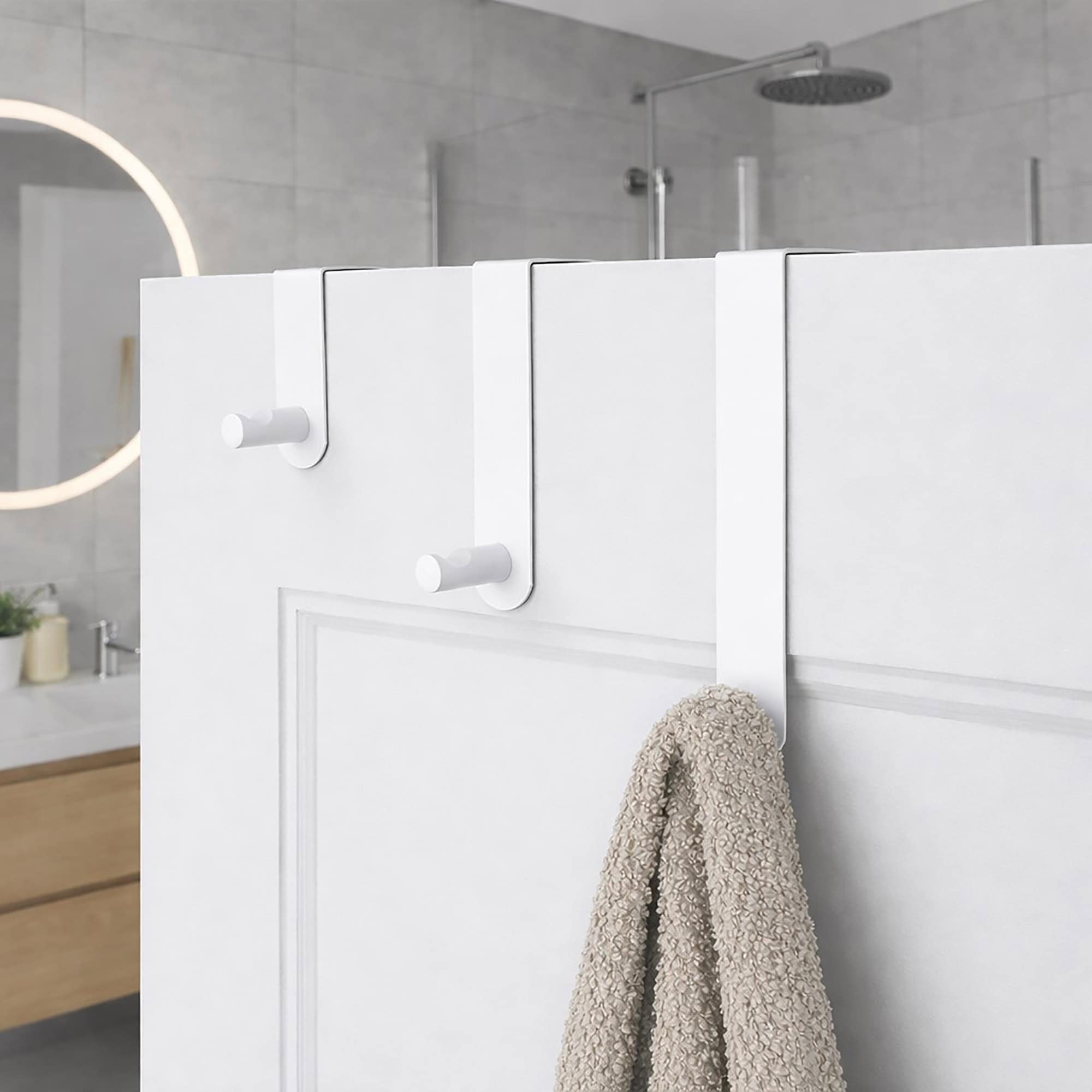 "Three white over-door hooks on white paneled bathroom door with beige towel hanging from lowest hook"