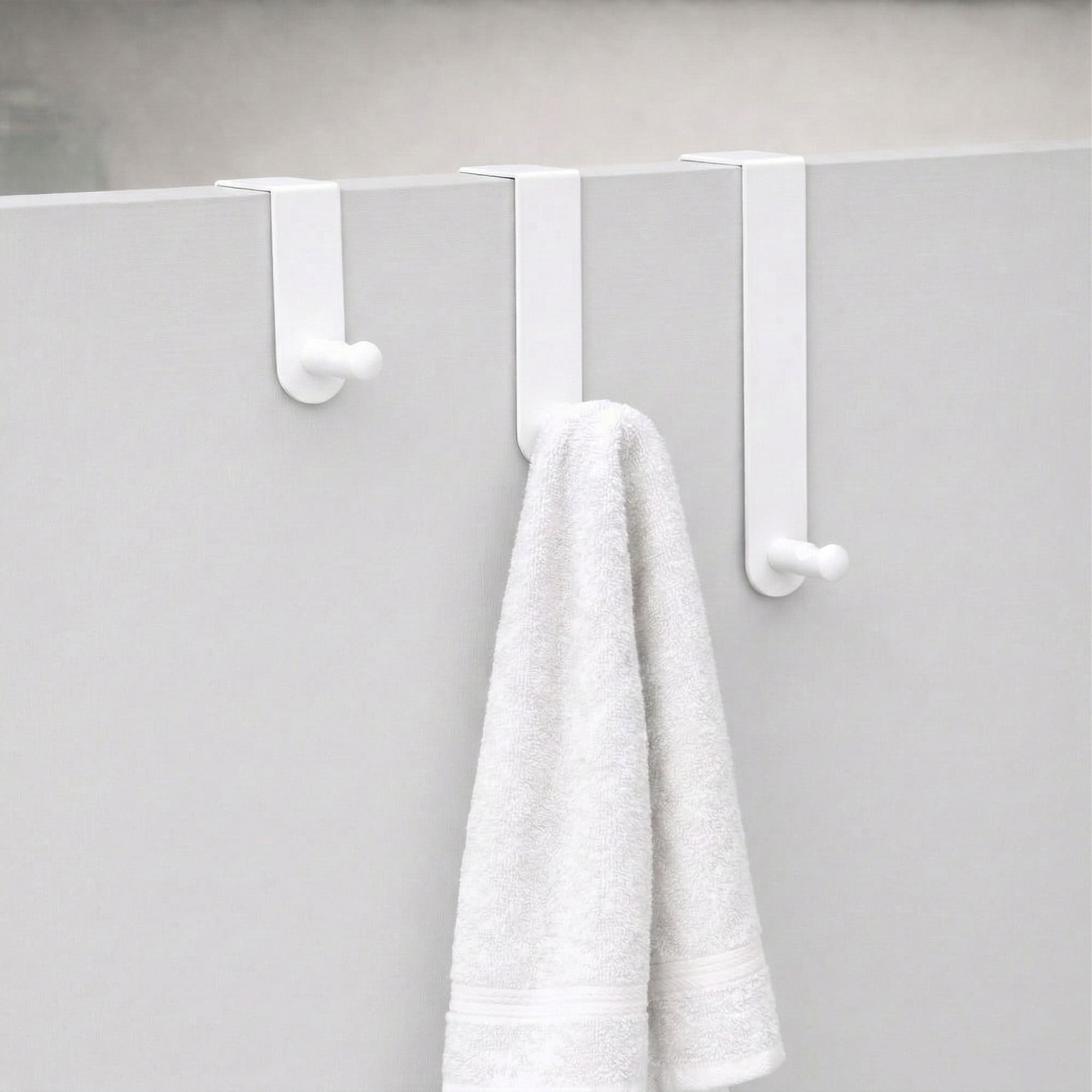 "Three white over-door hooks on gray door with white bath towel draped over middle hook"