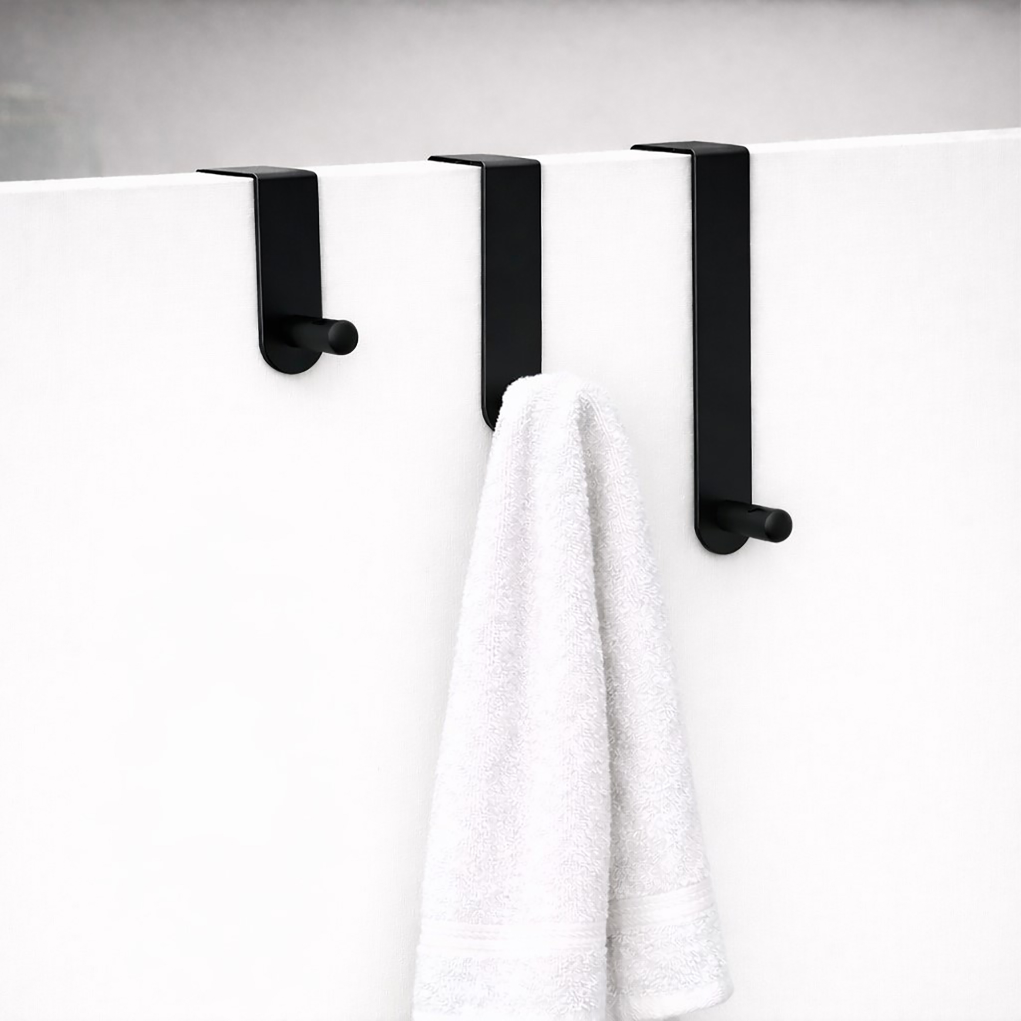 "Three matte black over-door hooks on white door with white bath towel draped over middle hook"