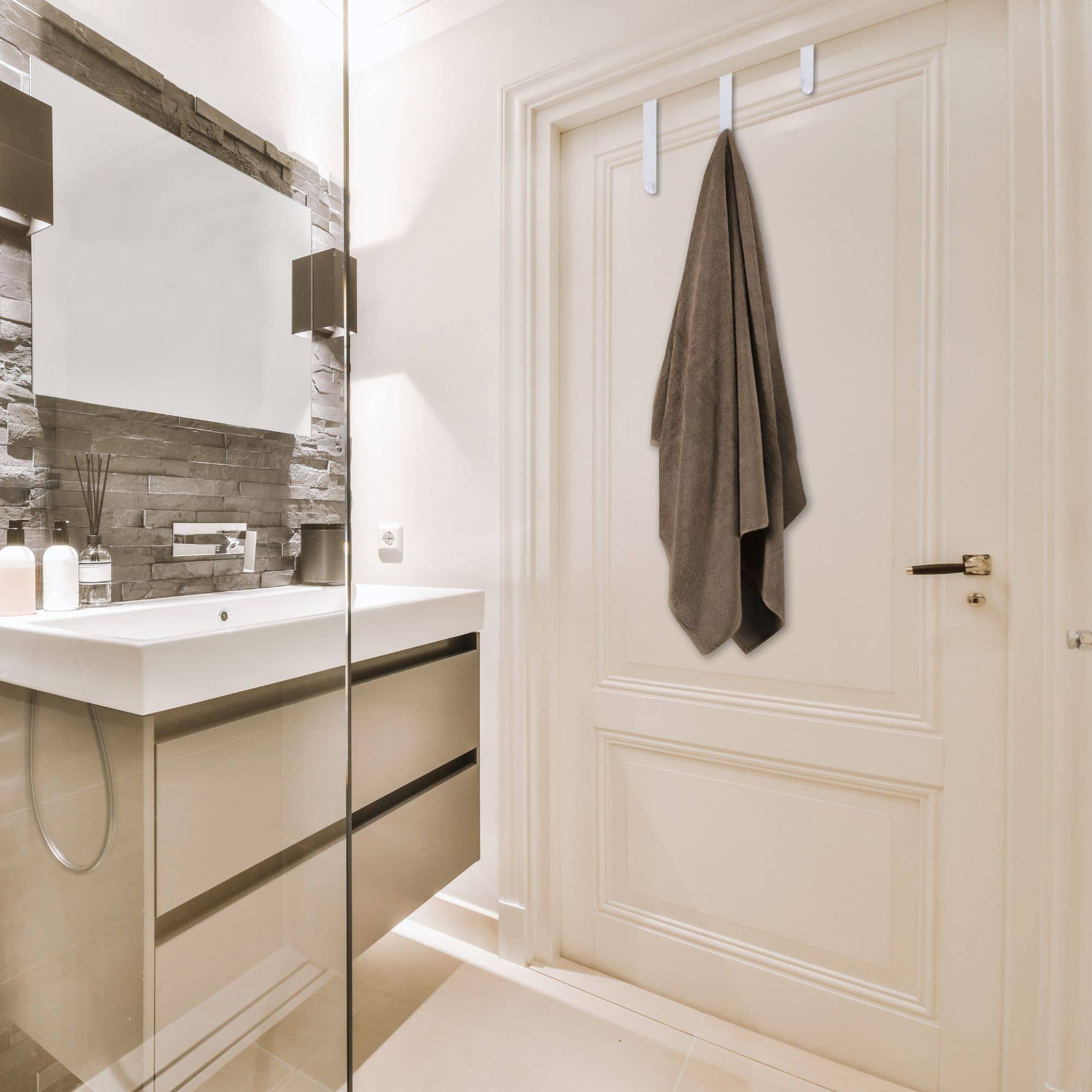 Elegant Bathroom Interior with a Set of White Over-the-Door Hooks Holding a Towel on a Classic White Door, Showcasing a Modern Vanity and Reflective Glass Shower.