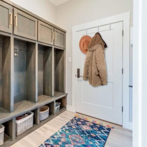 "White over-door hooks holding tan jacket and orange hat on white door in mudroom entryway"