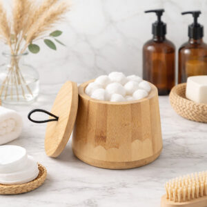 Natural bamboo cotton ball jar with lid and black loop on marble countertop with amber bottles and spa accessories