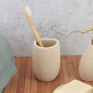 Sponge textured beige bathroom tumbler with toothbrush on wooden surface