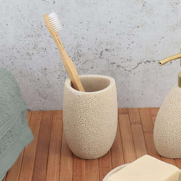 Sponge textured beige bathroom tumbler with toothbrush on wooden surface