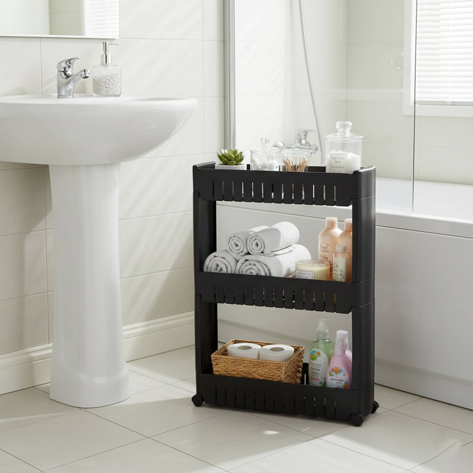Black 3-tier rolling cart holding rolled towels, bath products, and toilet paper in a white bathroom