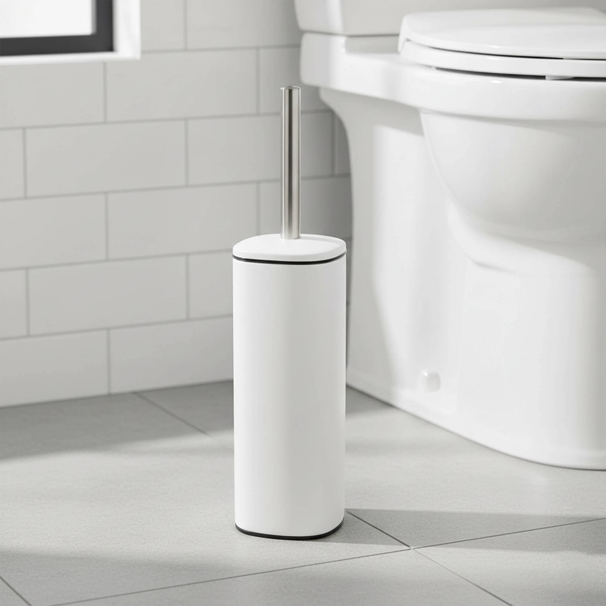 White square toilet brush with stainless steel handle and black trim beside white toilet in tiled bathroom