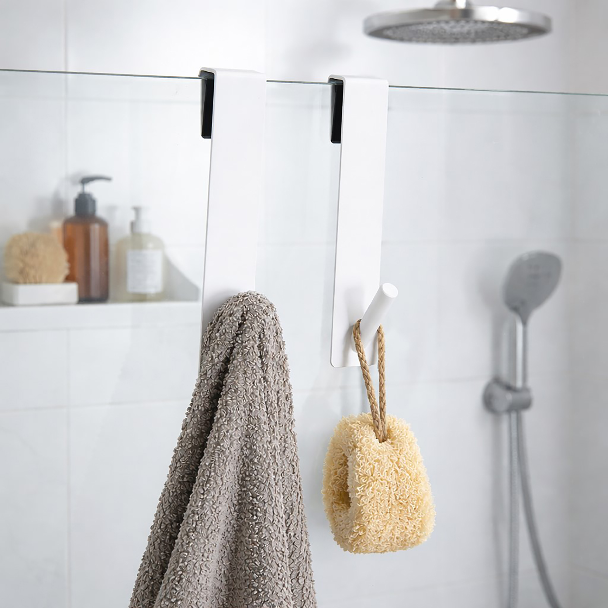 White over-the-shower-screen hooks, set of 2, holding a gray towel and a natural loofah on a glass shower panel.