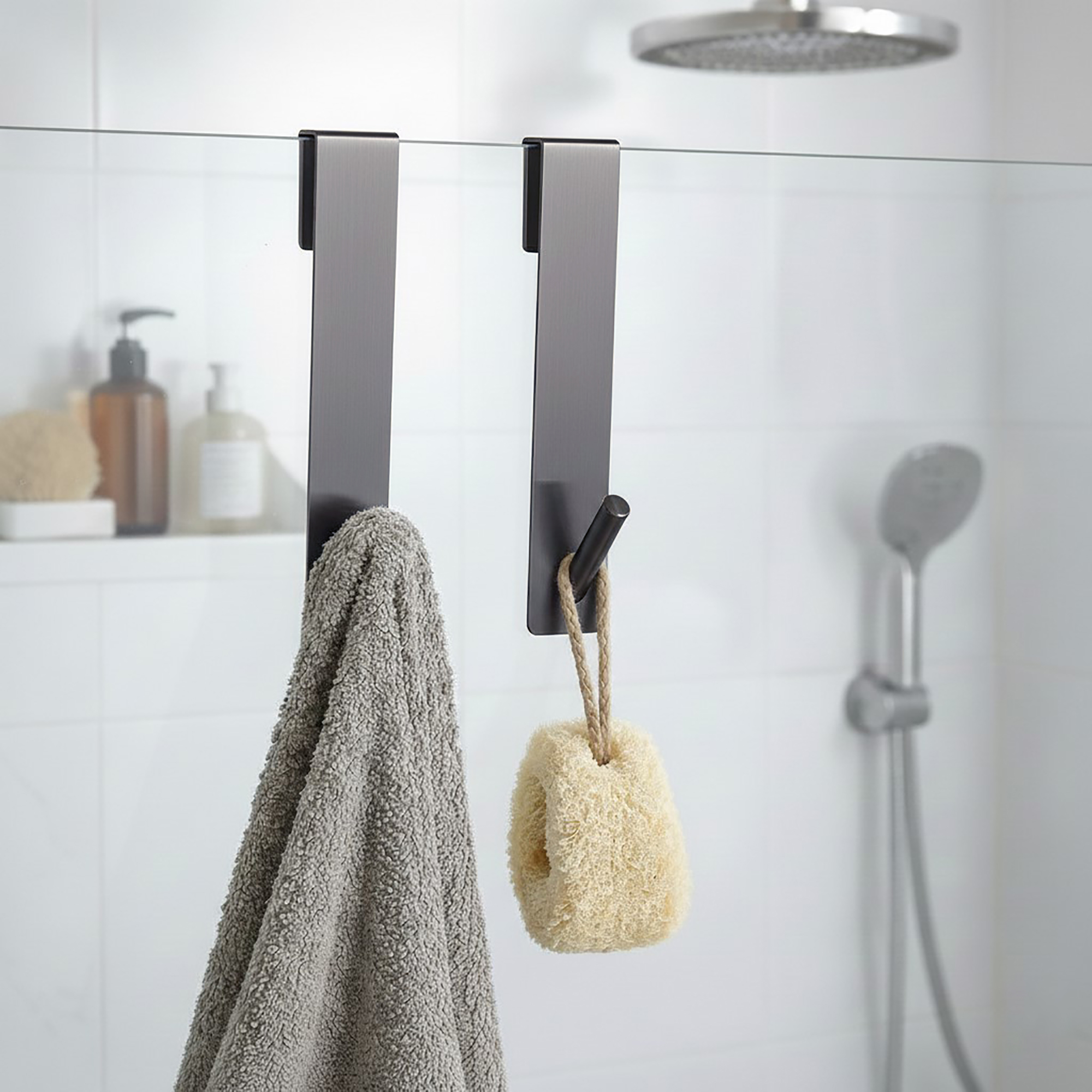 Chrome over-the-shower-screen hooks, set of 2, holding a gray towel and a natural loofah on a glass shower panel.