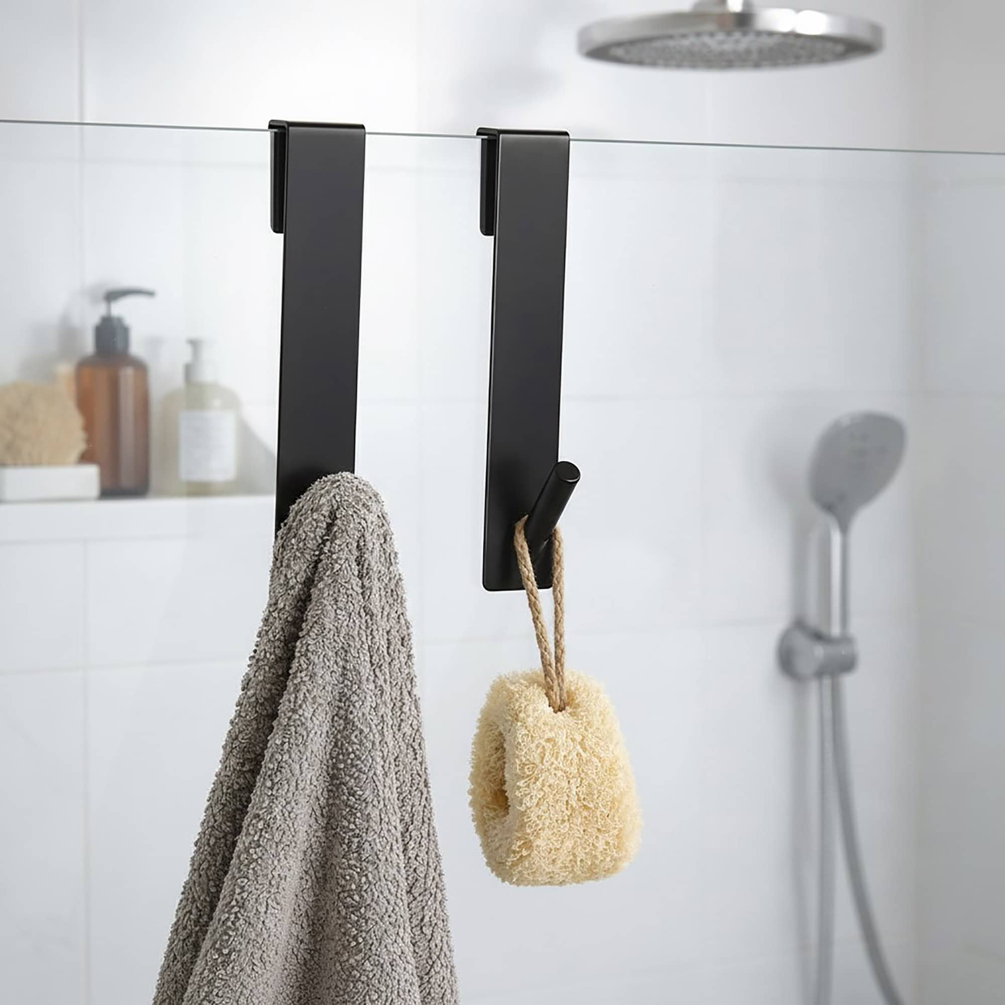 Black over-the-shower-screen hooks, set of 2, holding a gray towel and a natural loofah on a glass shower panel.