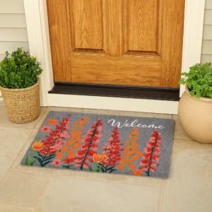 Gray welcome doormat with vibrant red and orange floral design at wooden front door