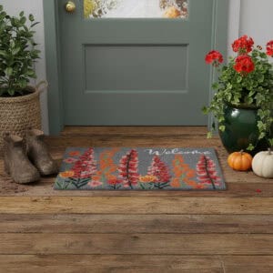 Floral welcome doormat with red and orange flowers placed at green door with fall decor