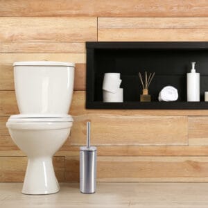 a chrome toilet brush set next to toilet seat in bathroom environment