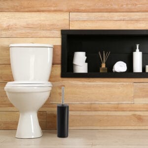 a black toilet brush set next to toilet seat in bathroom environment