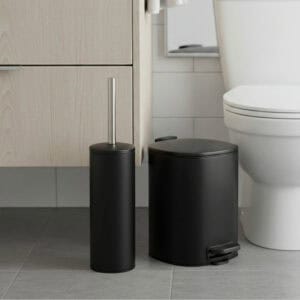 Black step trash can paired with matching toilet brush set near toilet