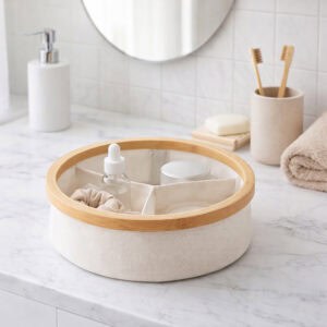 Image 3: Ecru round bamboo-rimmed 3-compartment basket holding skincare products and a scrunchie on a marble bathroom countertop.