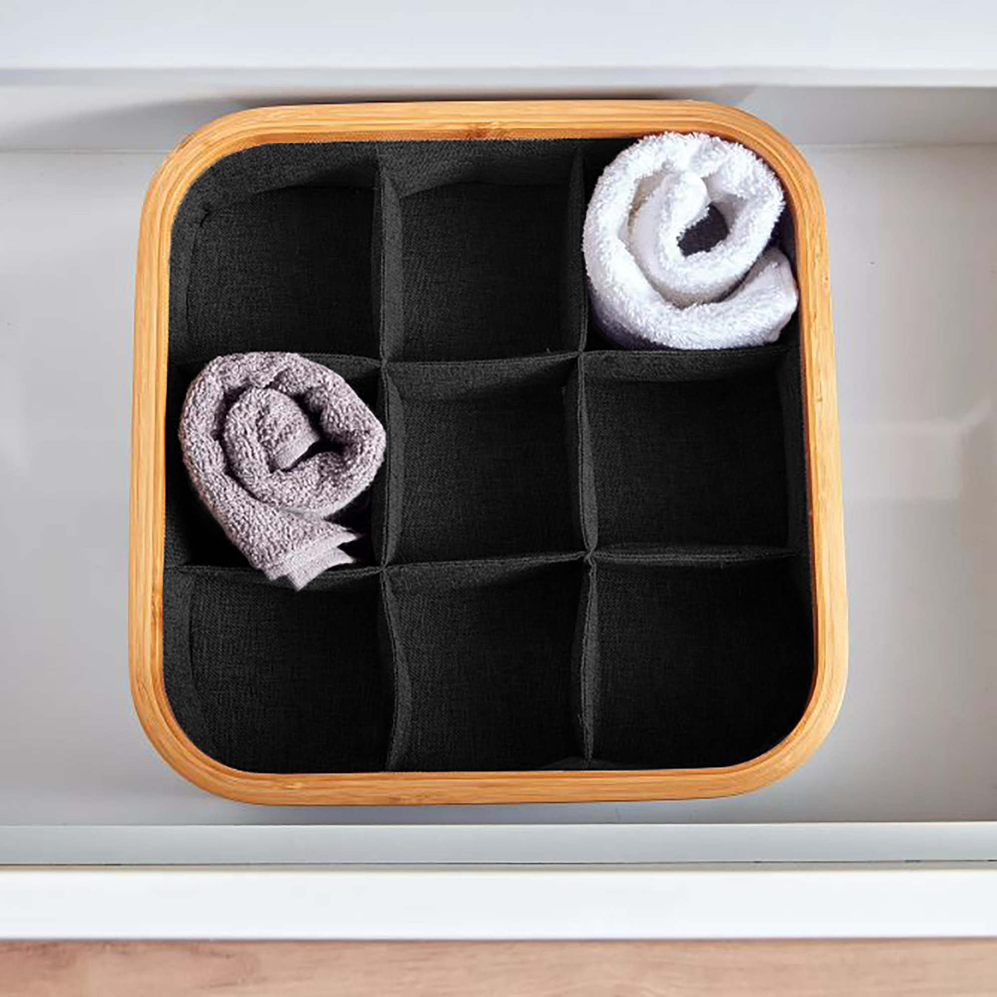 Image 3: Overhead view of a black 9-compartment bamboo-rimmed basket holding two rolled towels, placed inside a drawer.