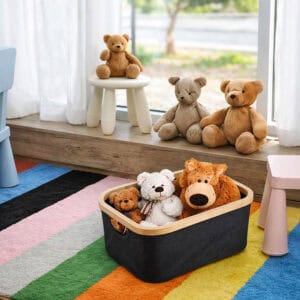 Black bamboo-rimmed storage basket filled with stuffed animal toys, placed on a colorful striped rug in a children's playroom.