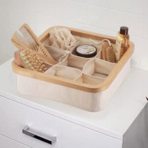 Image 6: Ecru 9-compartment bamboo-rimmed basket holding bath accessories including combs, brushes, body lotion, and shower gel on a white dresser.