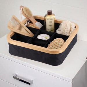 Image 8: Black 9-compartment bamboo-rimmed basket holding bath accessories including combs, brushes, shower gel, and a loofah on a white dresser.