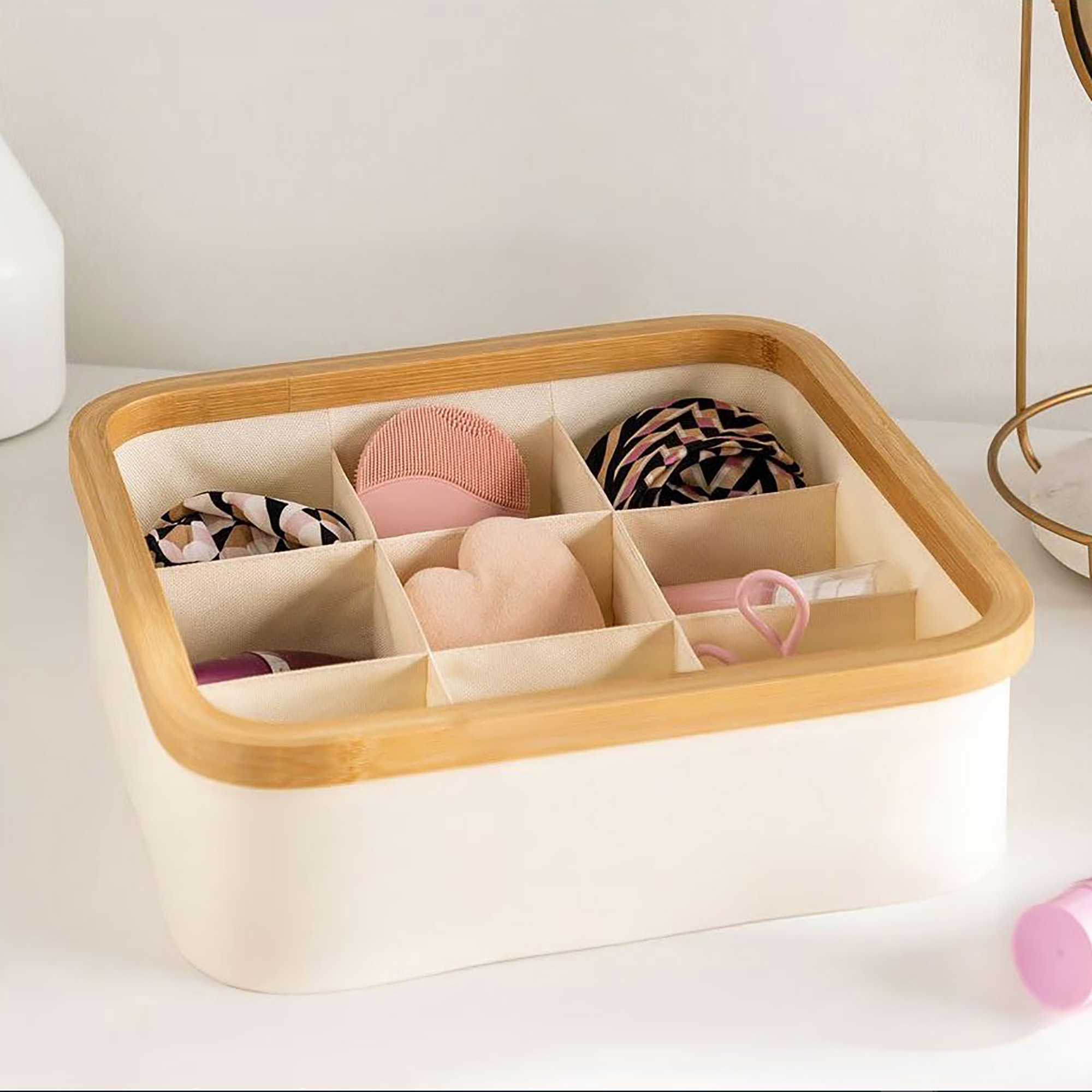 Image 8: Ecru bamboo-rimmed 9-compartment basket organizing makeup accessories including a facial brush, hair ties, and beauty sponge on a vanity.
