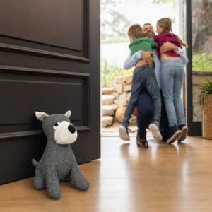 Charcoal dog door stopper propping open a dark paneled door on hardwood floor, with a family embracing in the doorway behind.
