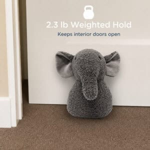 Grey elephant door stopper propping open a white door on carpet, with a kettlebell icon. On-image text: "2.3 lb Weighted Hold," "Keeps interior doors open."