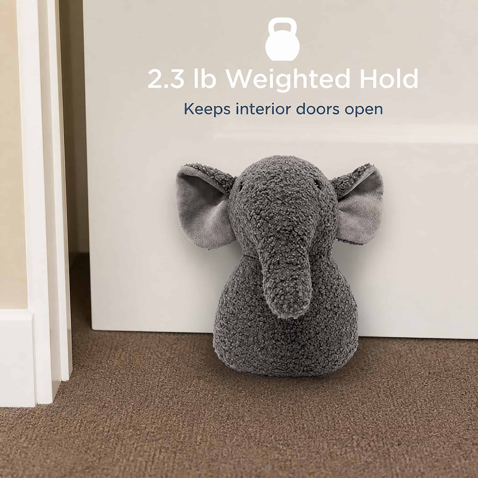 Grey elephant door stopper propping open a white door on carpet, with a kettlebell icon. On-image text: "2.3 lb Weighted Hold," "Keeps interior doors open."