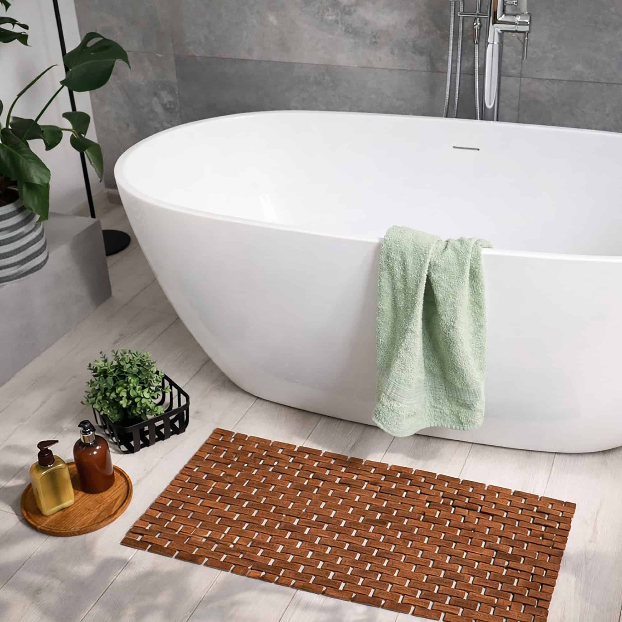 Bamboo bath mat placed beside white freestanding bathtub with green towel