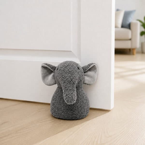 Grey elephant door stopper propping open a white paneled door on hardwood floor, sofa in the background.