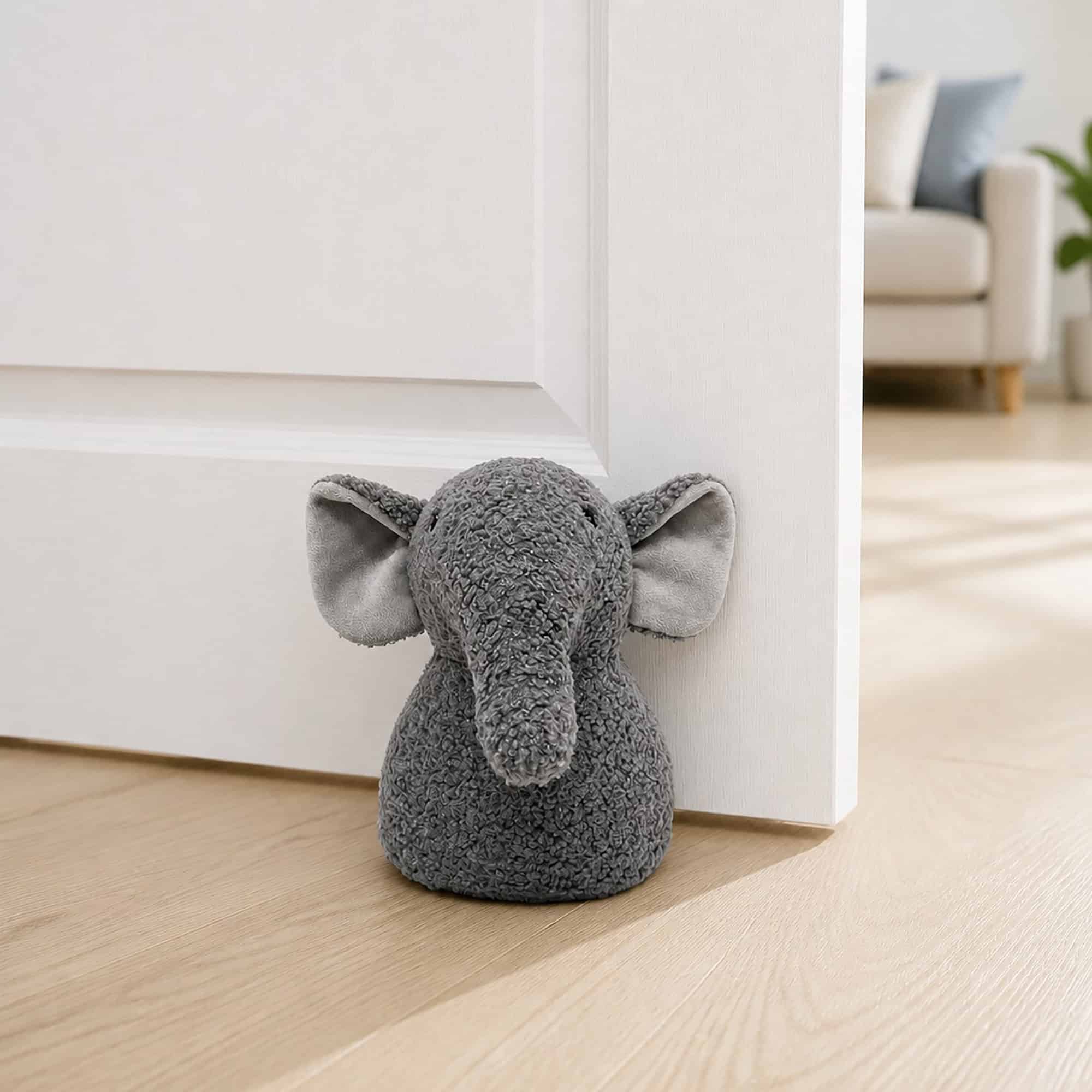Grey elephant door stopper propping open a white paneled door on hardwood floor, sofa in the background.
