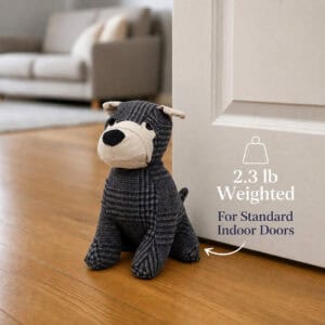Charcoal plaid dog door stopper propping open a white door on hardwood floor, sofa behind, with a weight icon. On-image text: "2.3 lb Weighted," "For Standard Indoor Doors."