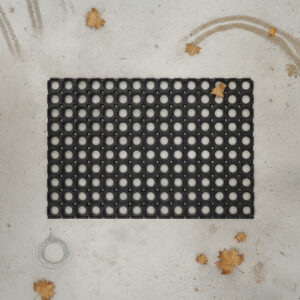 "Black rubber open-grid doormat on concrete surrounded by fallen autumn leaves and raindrops"