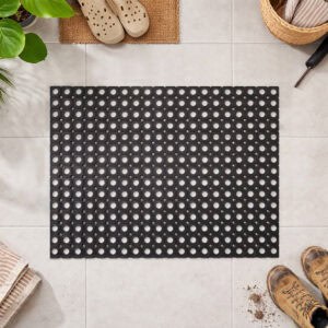 Black rubber ring mat with circular holes on a tiled floor, surrounded by shoes and garden tools.